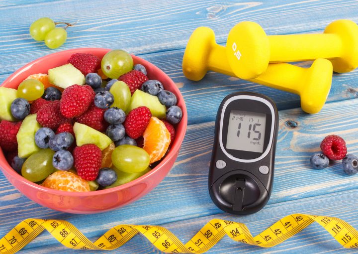 Fresh fruit salad, glucose meter with result of sugar level, tape measure and dumbbells for fitness, concept of diabetes, sport, slimming, healthy lifestyles and nutrition